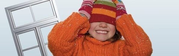 Sapkás kislány takarja el a szemét egy műanyag ablakkeret mellett