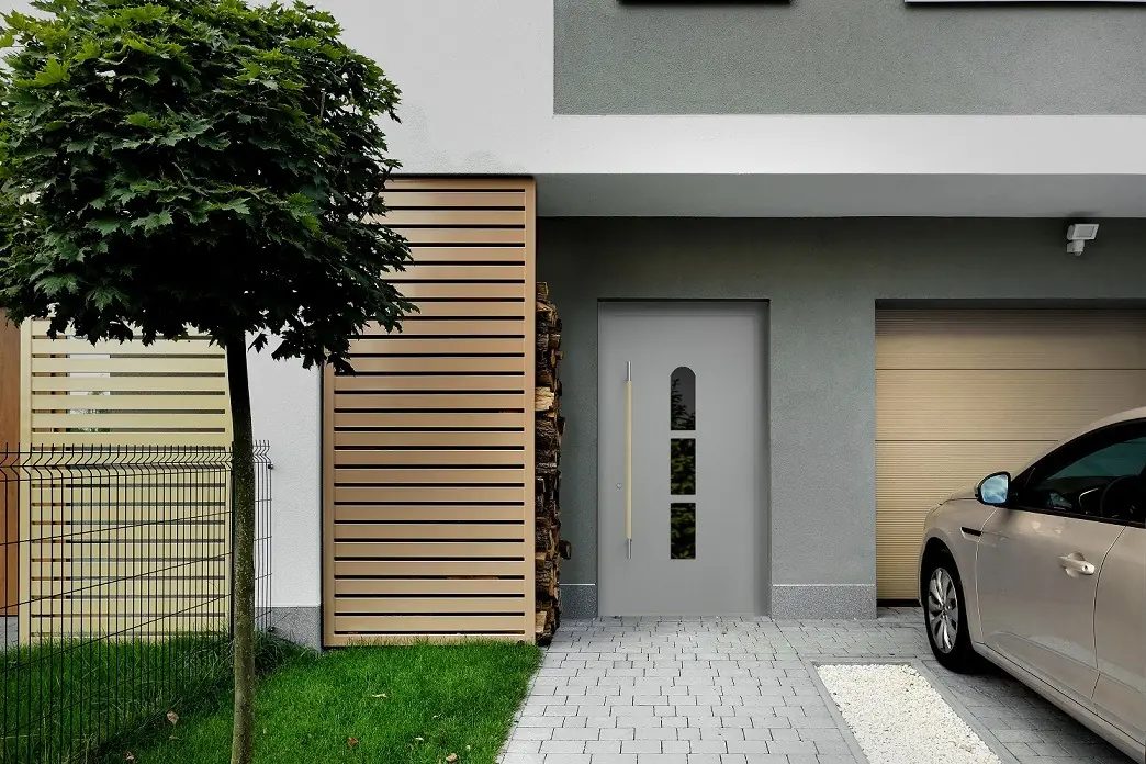 Szürke bejárati ajtó egy modern ház előtt, mellette garázskapu